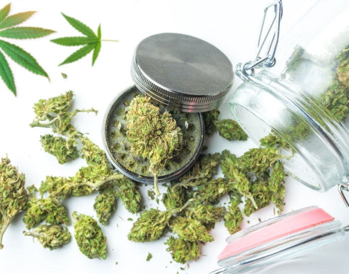 Cannabis buds with grinder and glass jar on white background for medical and recreational use.