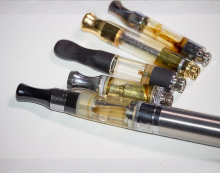 Cannabis vape cartridges with oil extracts and metal vape pen on white background.