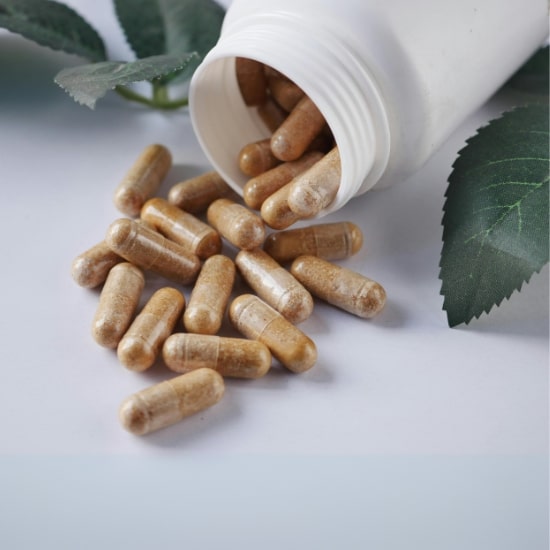 Herbal supplement capsules spilling from bottle with natural leaf background.