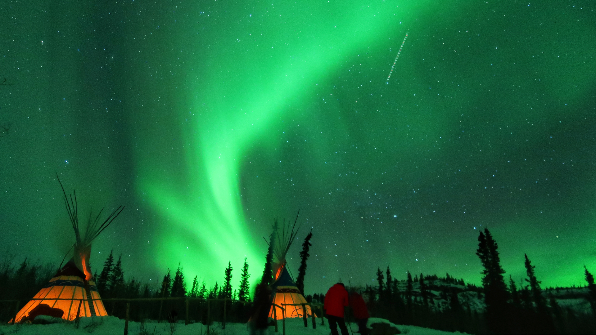 Aurora Borealis glowing over frozen lake and forest in Northern Canada.