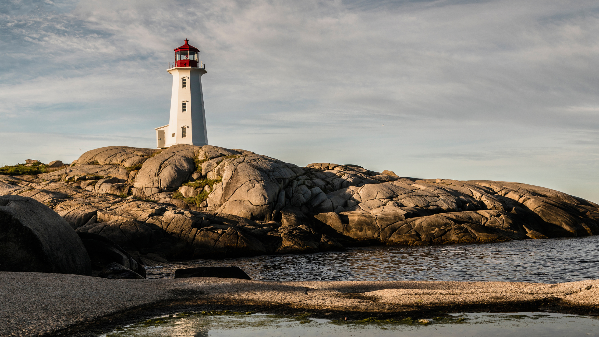 Peggy’s Cove Lighthouse in Nova Scotia on rocky shore under a golden evening sky