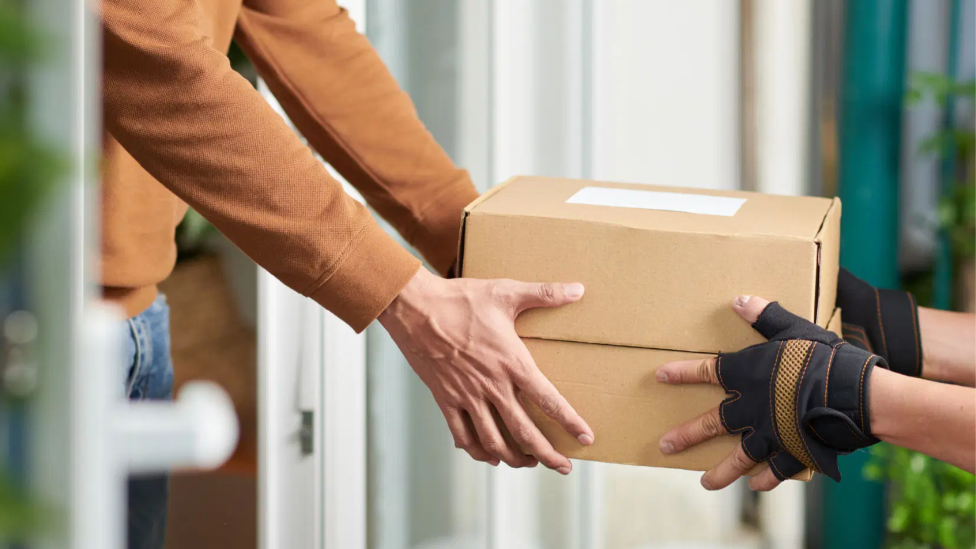 A delivery person handing over a cardboard package to a woman at her doorstep.